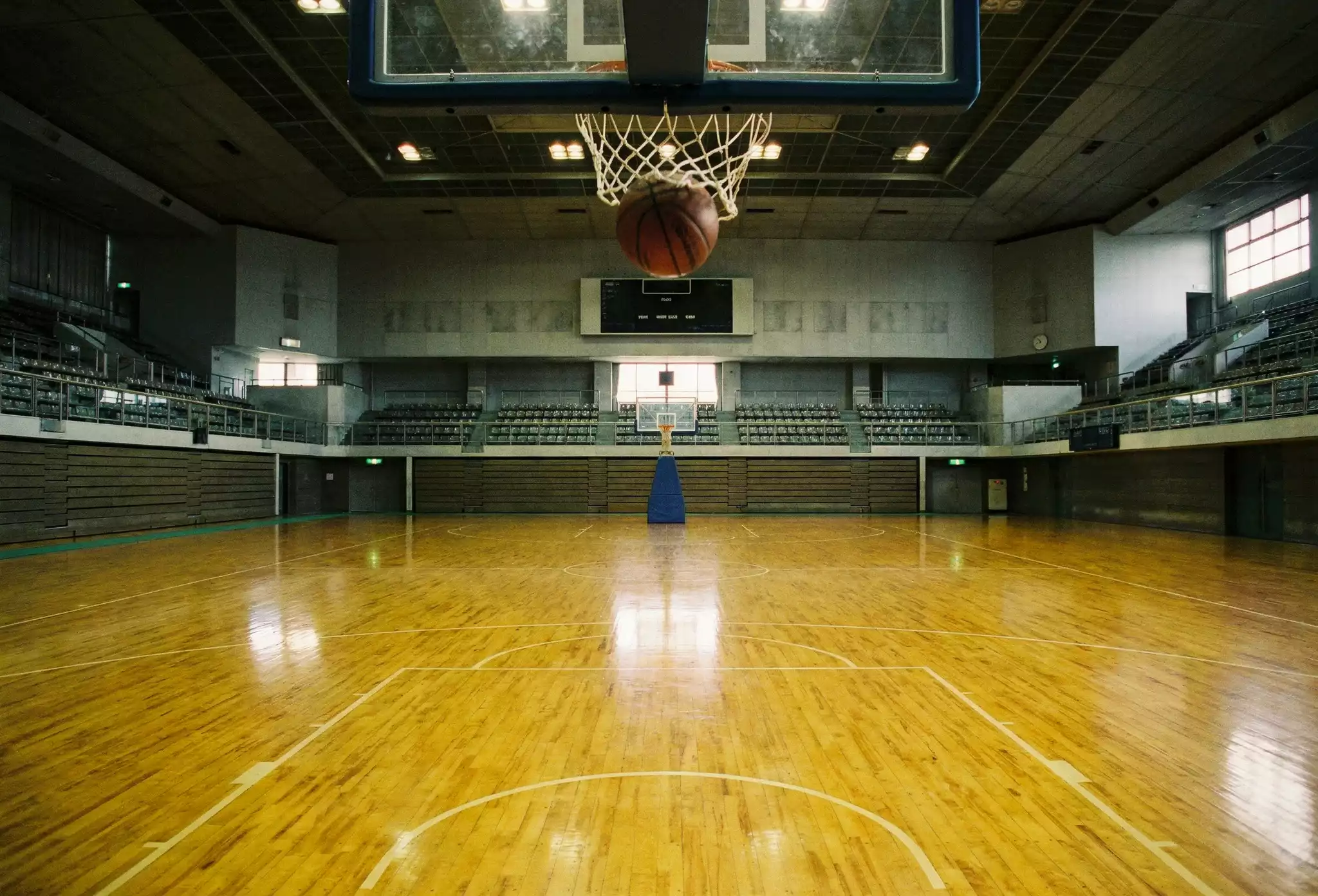 Bola de basquetebol junto ao aro num pavilhão com piso de madeira envernizada