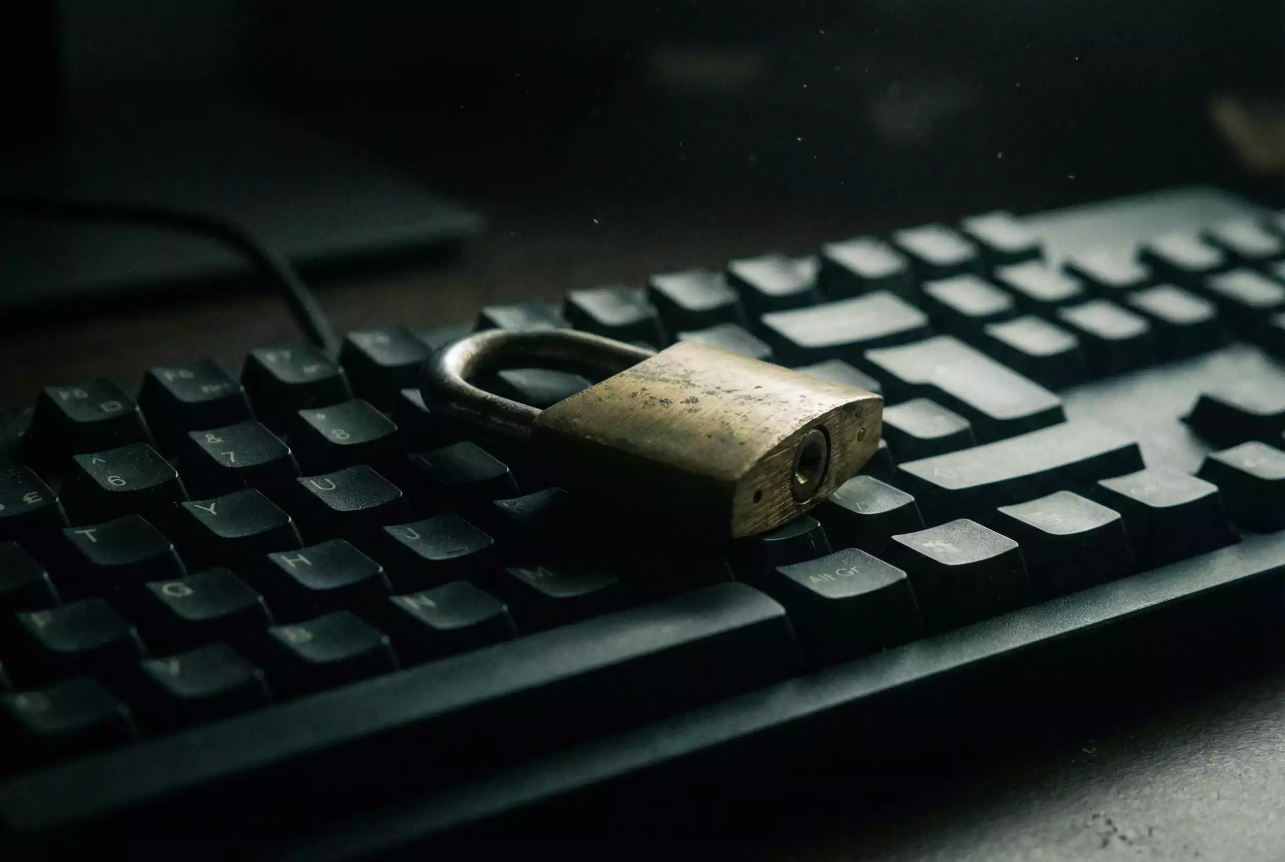 Cadeado fechado sobre um teclado de computador num ambiente escuro