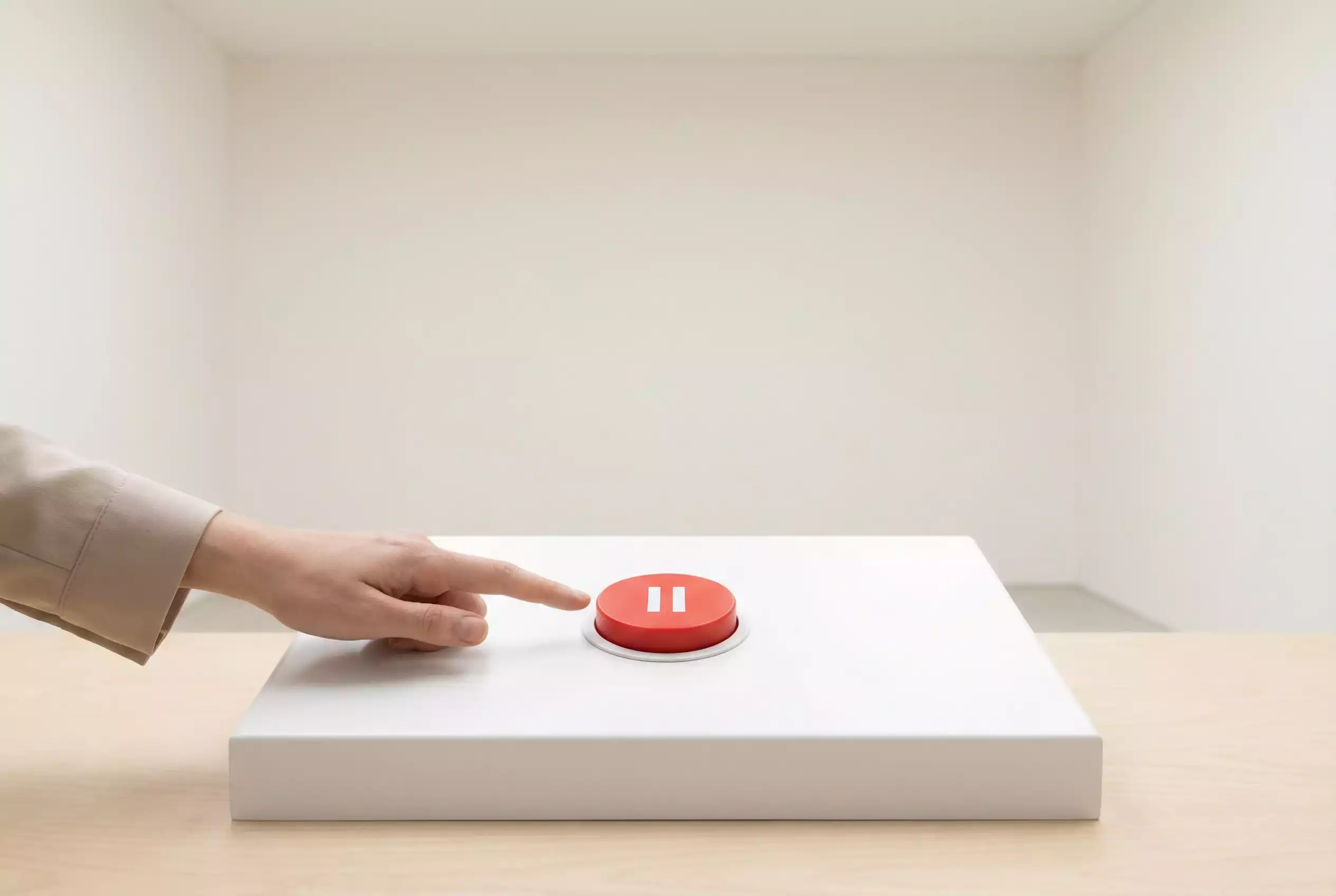 Mão a premir um botão vermelho de pausa sobre um painel branco