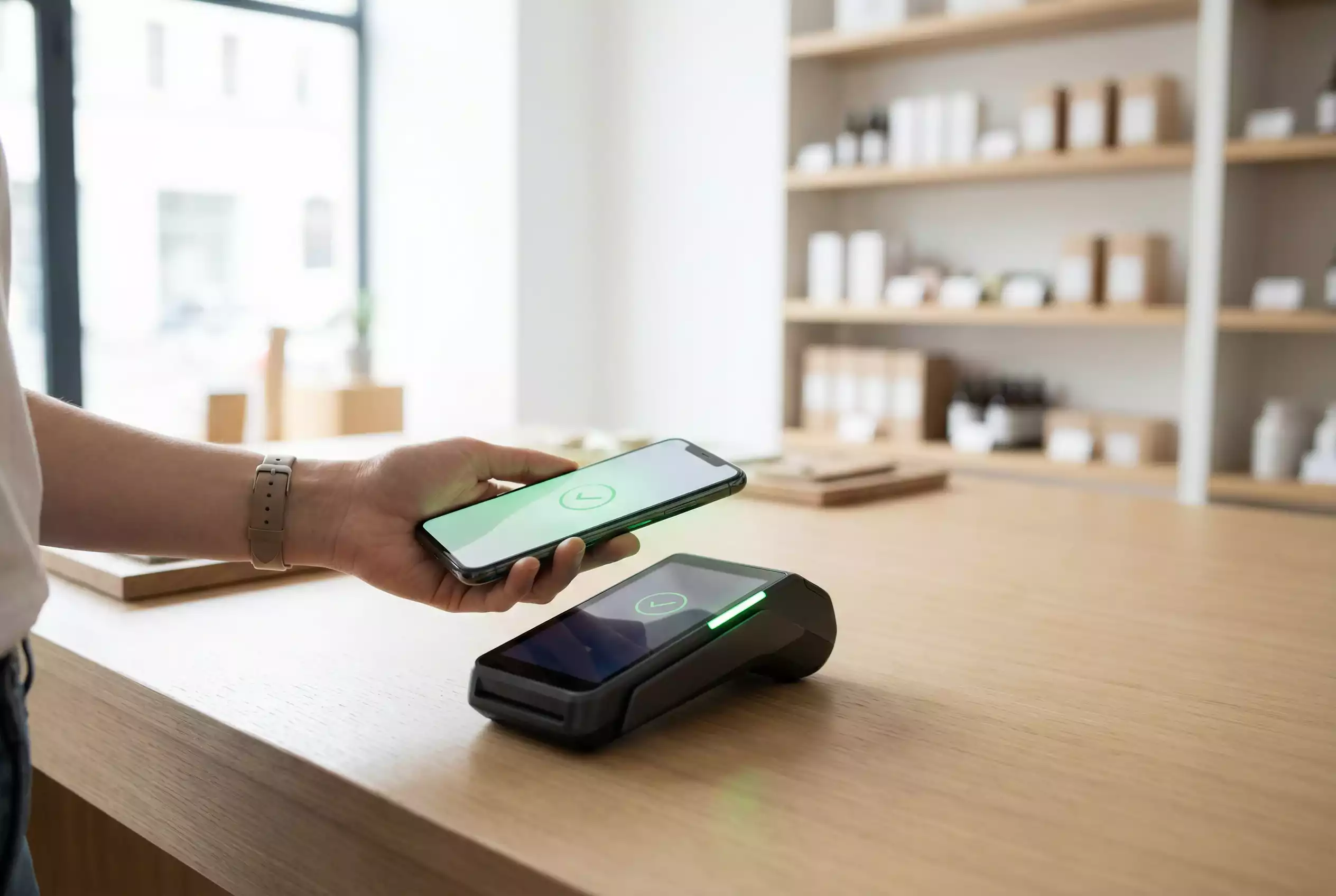 Mão a segurar um smartphone com ecrã de pagamento junto a um terminal contactless